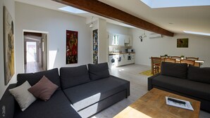 A modern living room with a sofa, a coffee table, and a dining area with a table and chairs. There is a kitchen in the background with white cabinets and a microwave. - Villa St Simon (Blaye)