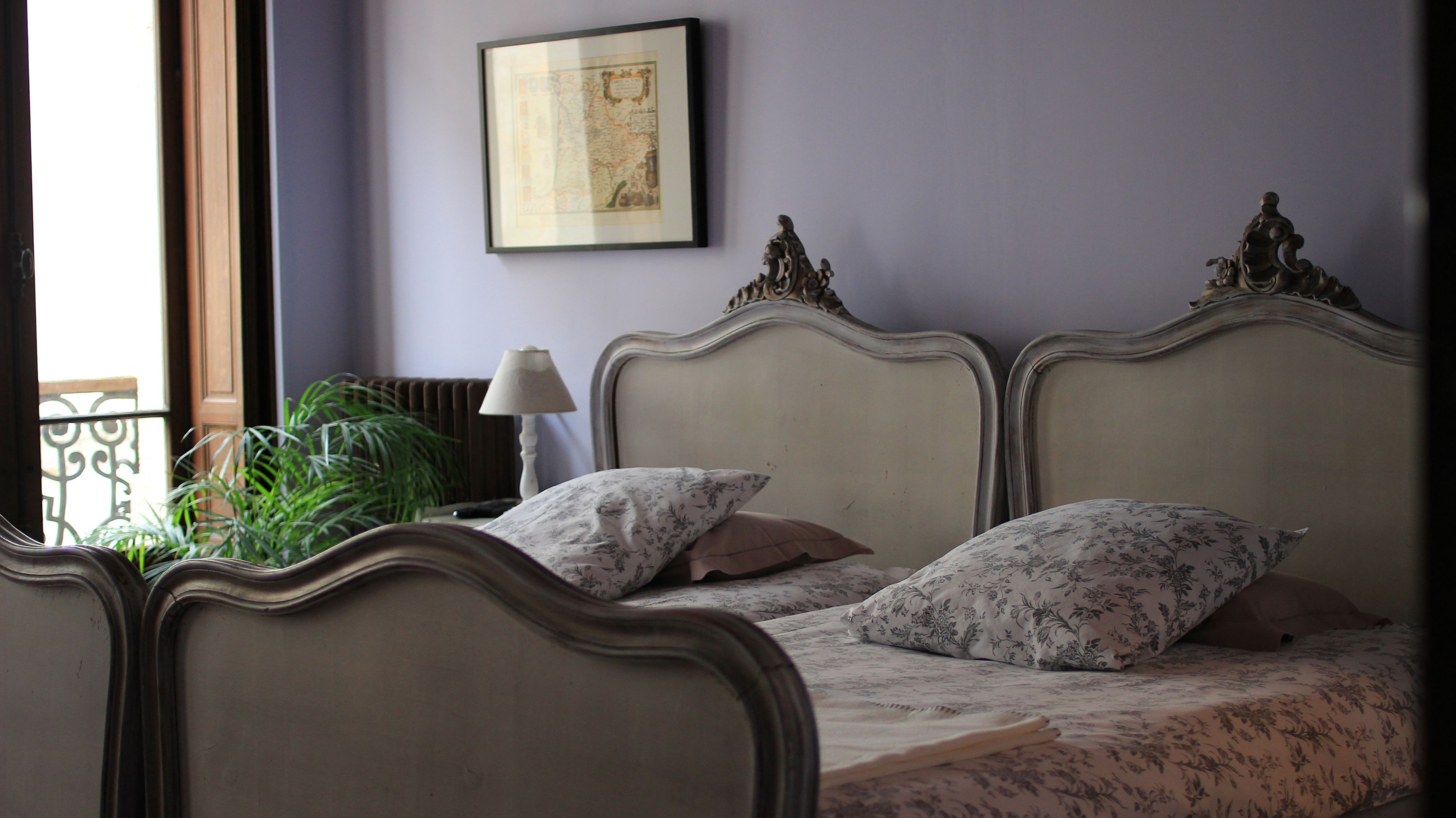 Una cama con cabeceros decorados, un mapa enmarcado en la pared y una planta en maceta junto a la ventana.