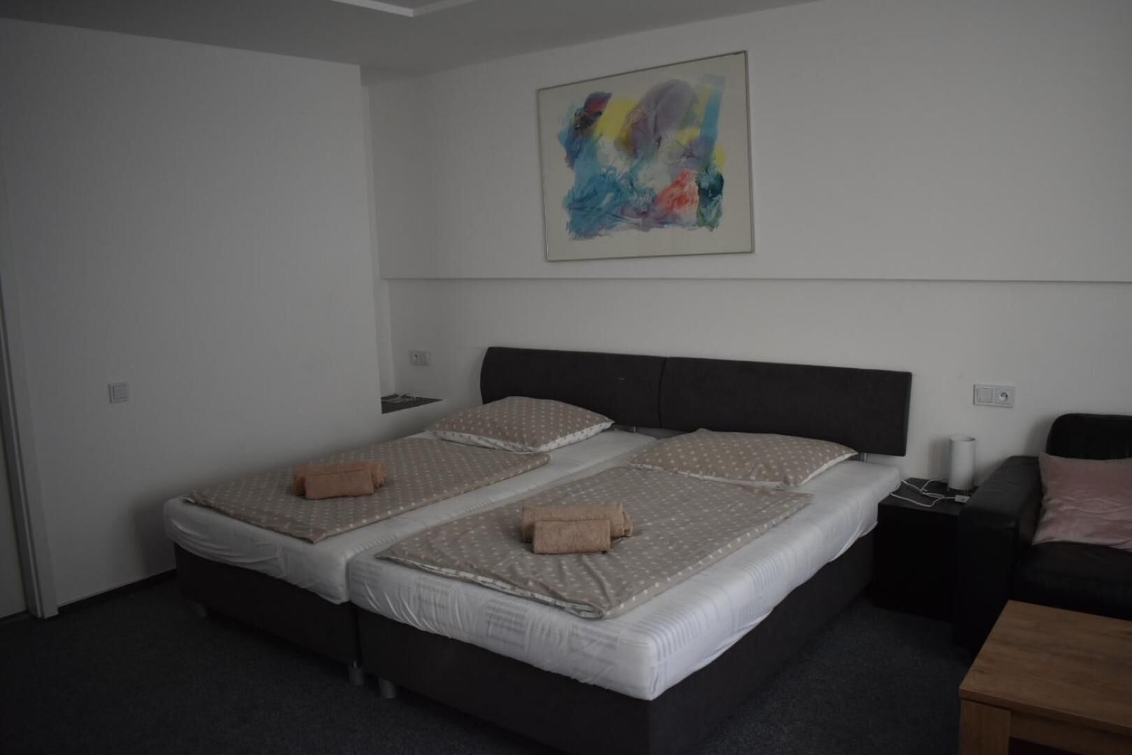A double bed with two pillows and a blanket, a bedside table with a lamp, and a small wooden table.