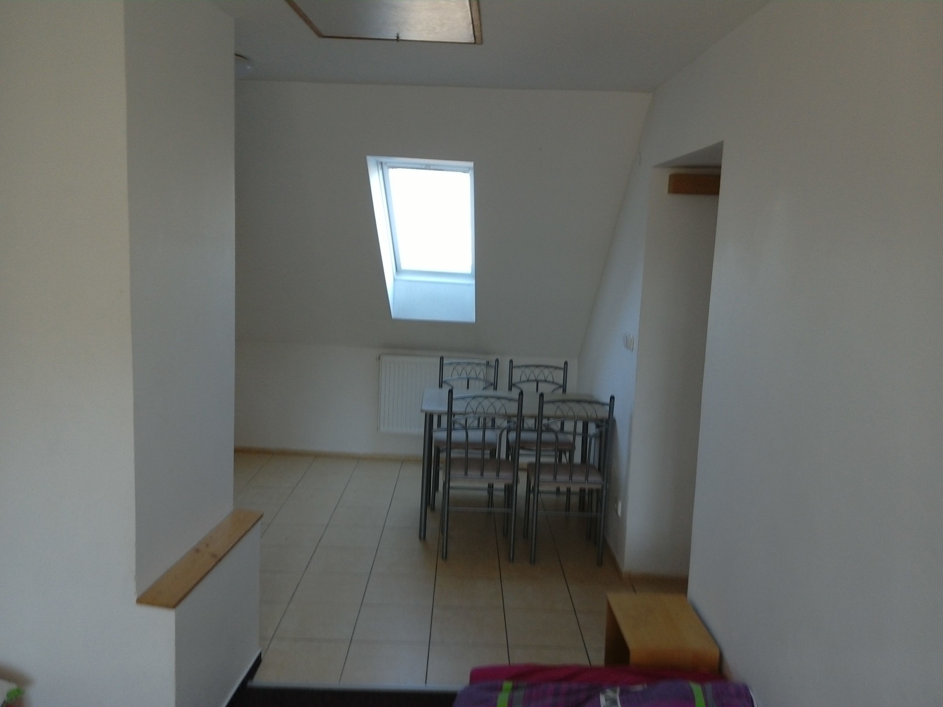 Une pièce avec un plafond en pente, une lucarne, un lit et une table à manger avec des chaises.