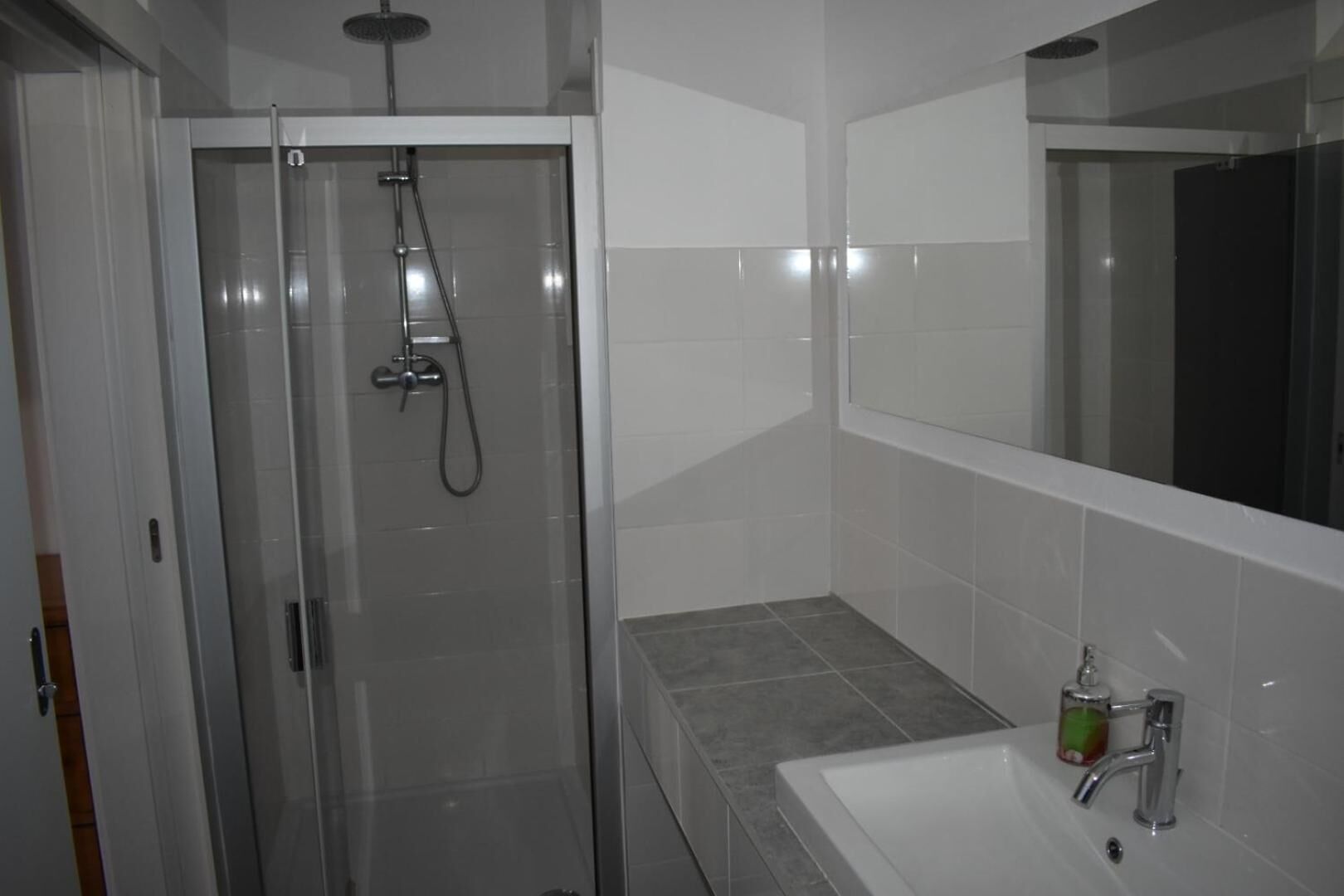 Un baño moderno con ducha envuelta en vidrio, un lavabo blanco y un espejo grande.