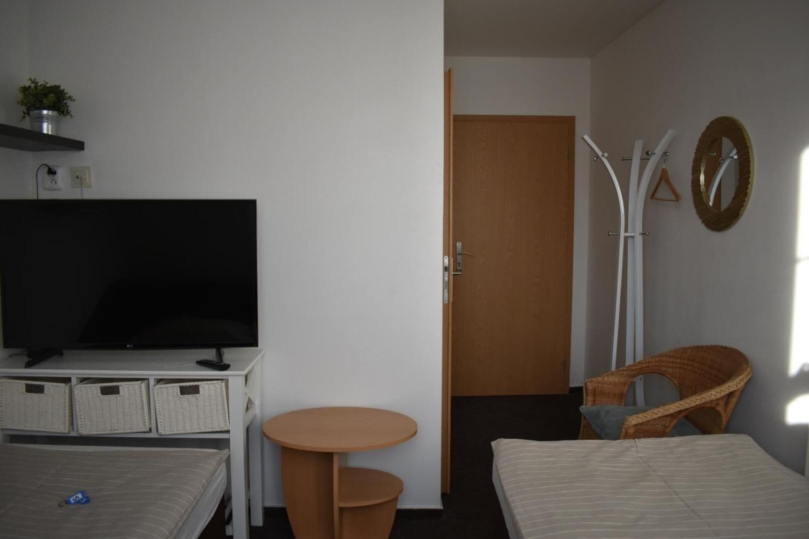 Quarto de hotel com televisão, duas camas, uma mesinha, uma cadeira e uma porta.