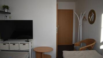 Quarto de hotel com televisão, duas camas, uma mesinha, uma cadeira e uma porta.