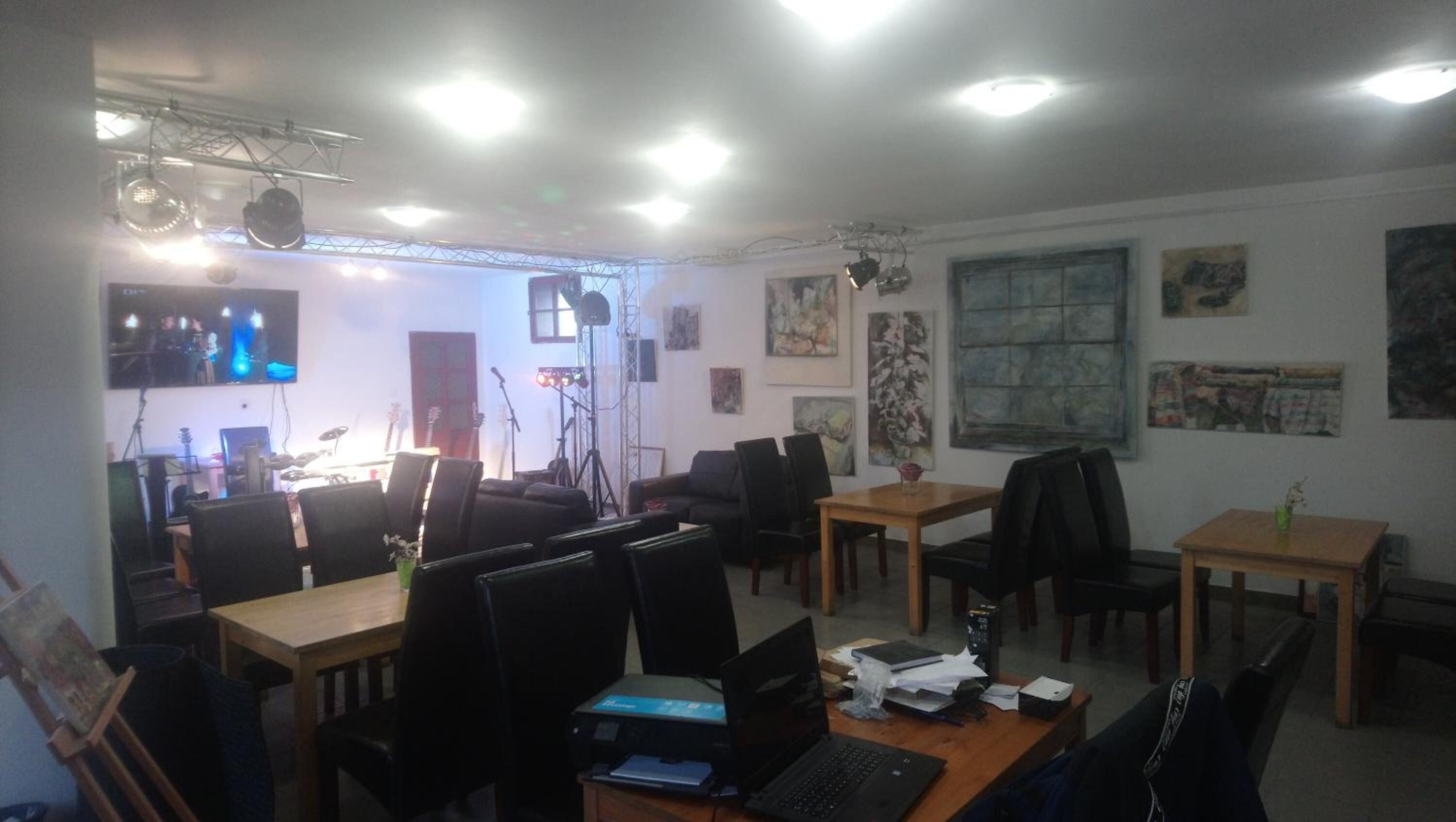 A room with multiple tables and chairs, a stage with musical instruments, and artwork on the walls.
