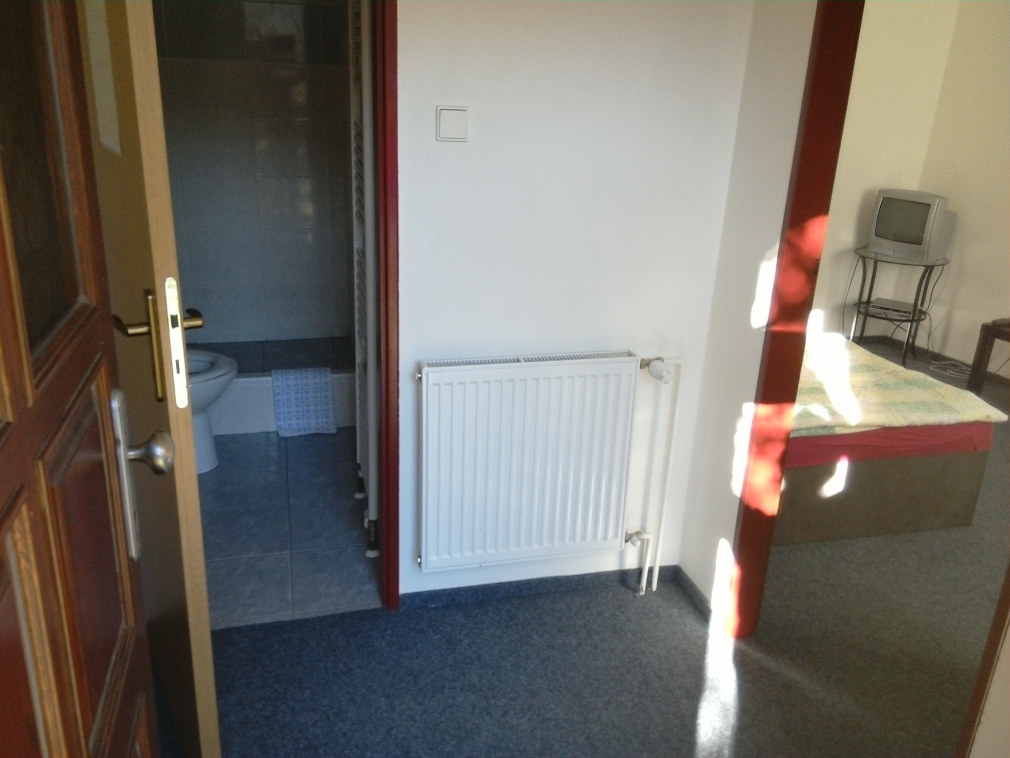 Une pièce avec un radiateur, une petite table et une chaise, et un téléviseur posé sur un meuble.