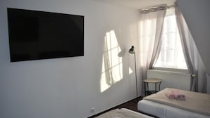 Een slaapkamer met twee bedden, een aan de muur bevestigde televisie, een vloerlamp en een raam met gordijnen.