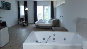 Una habitación de hotel moderna con una bañera grande, una cama redonda, un sofá y un televisor en la pared.