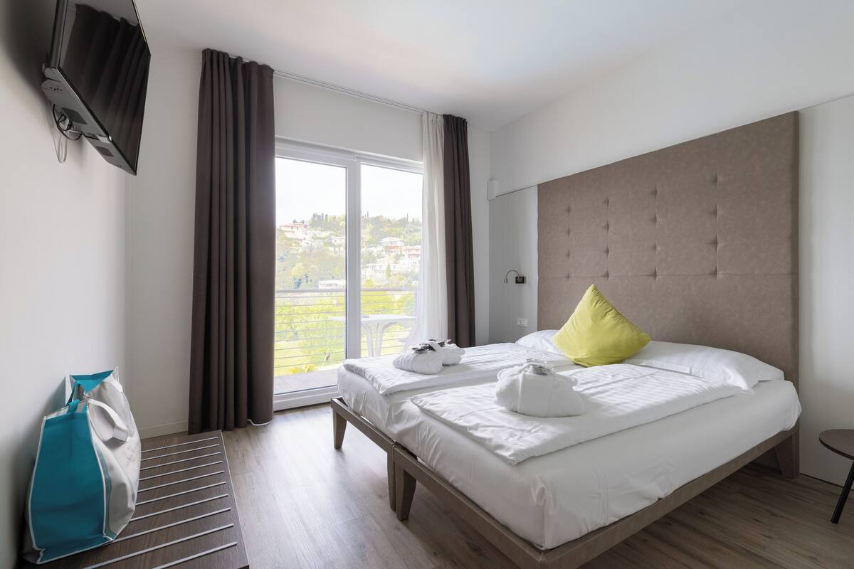 Ein Hotelzimmer mit einem großen Bett, einer Bank, einem Fernseher und Blick ins Freie.