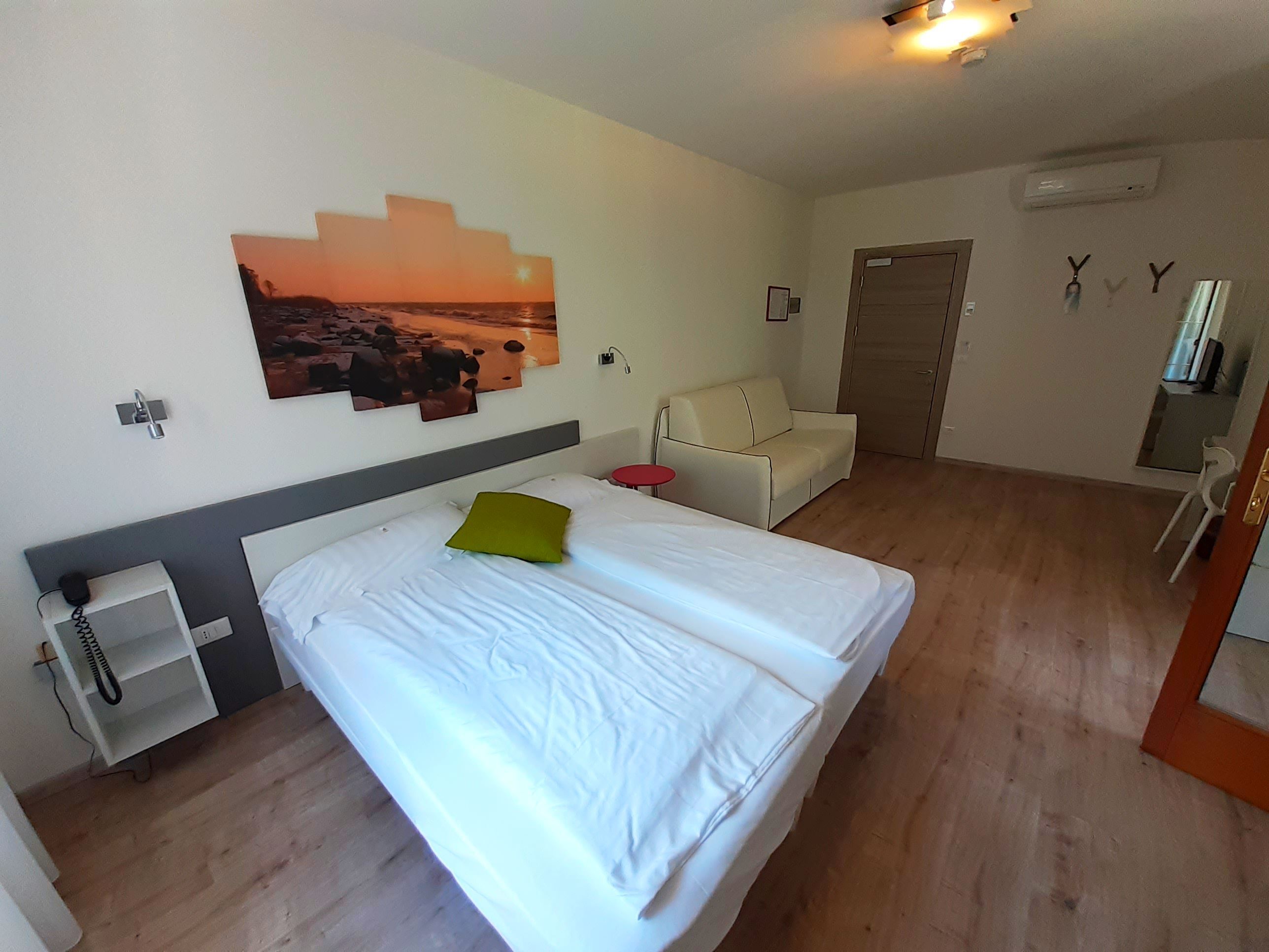 A hotel room with a bed, a small table, a sofa, and a wall-mounted TV.