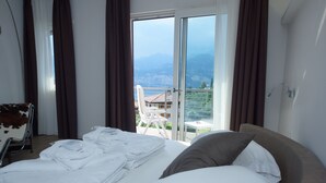 Habitación de hotel con una cama, una silla y vistas a las montañas y al agua.