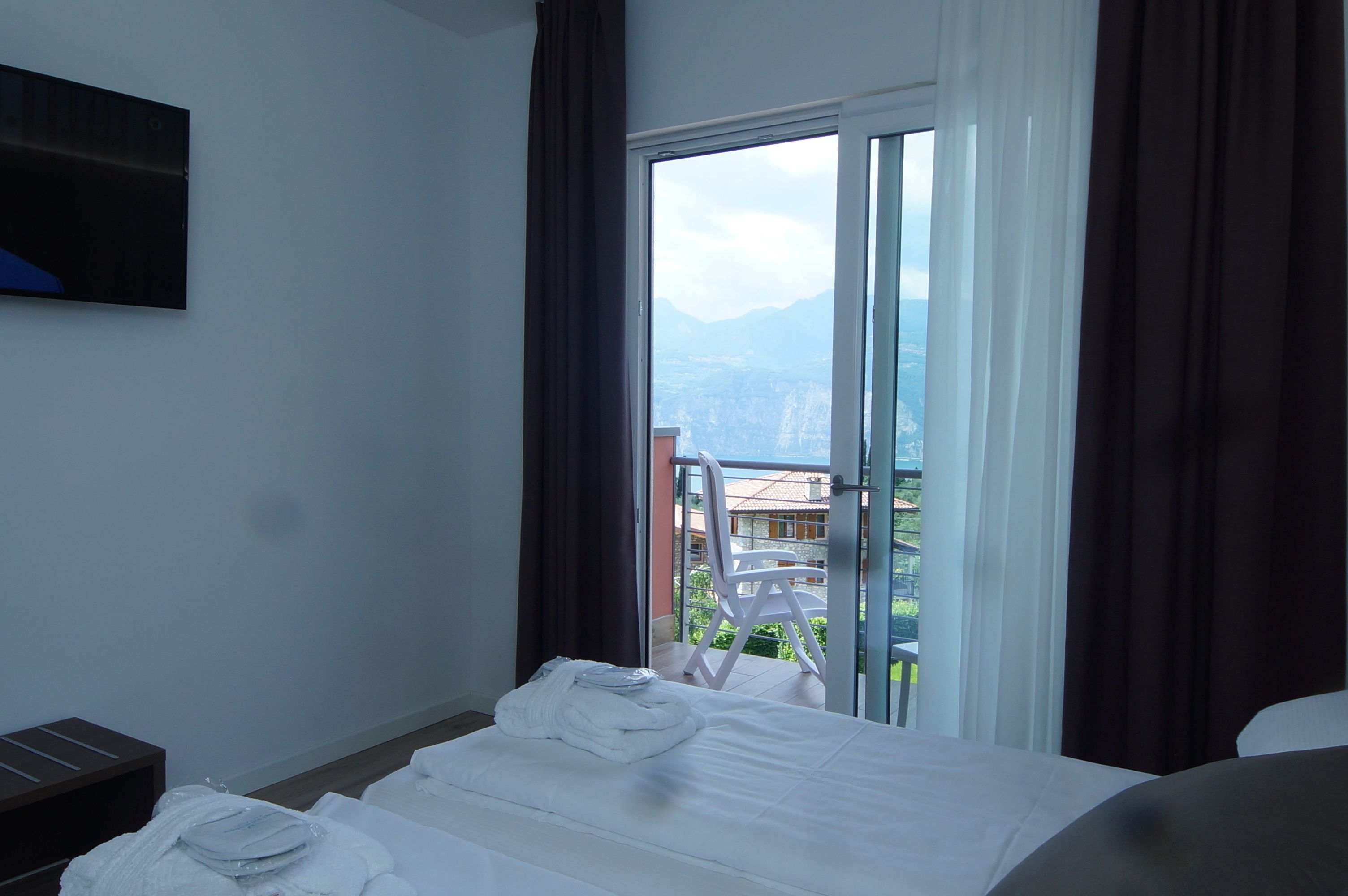 Une chambre d’hôtel avec un lit, un téléviseur fixé au mur et une vue sur les montagnes par une grande fenêtre.