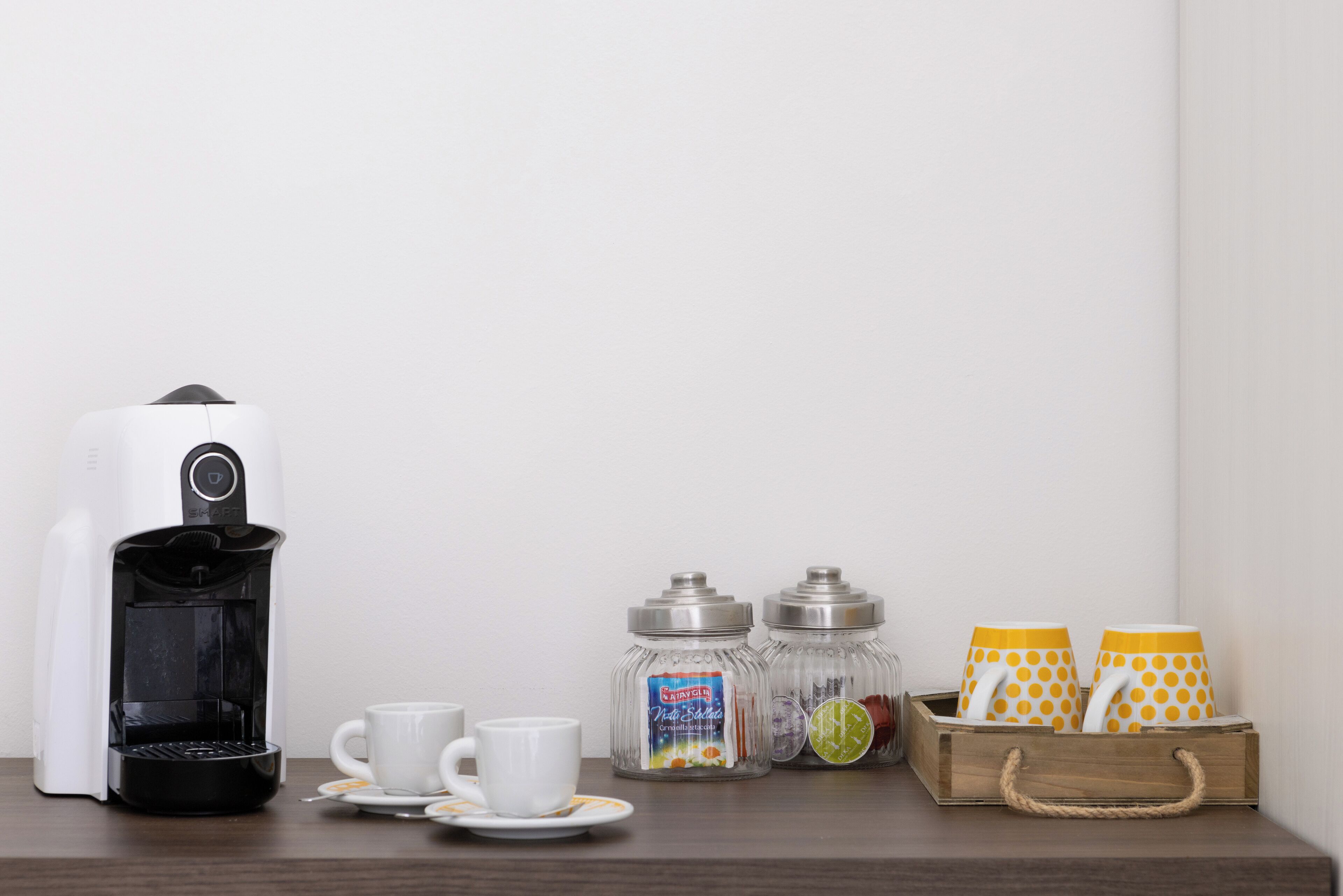 A coffee maker, two cups, two salt shakers, and a tray with polka-dotted cups on a wooden table.