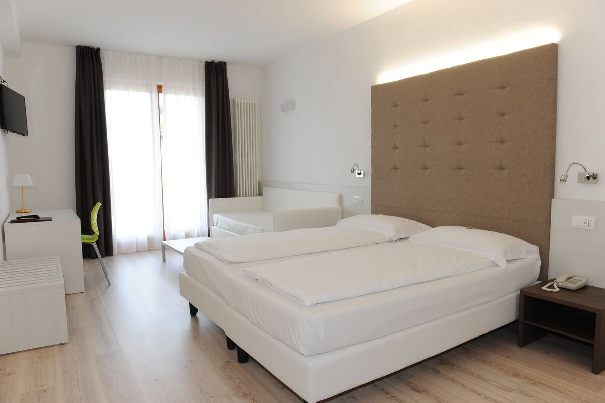 Ein Hotelzimmer mit zwei Betten, einem Schreibtisch, einem Sessel, einem Fernseher und einem Nachttisch mit Telefon.