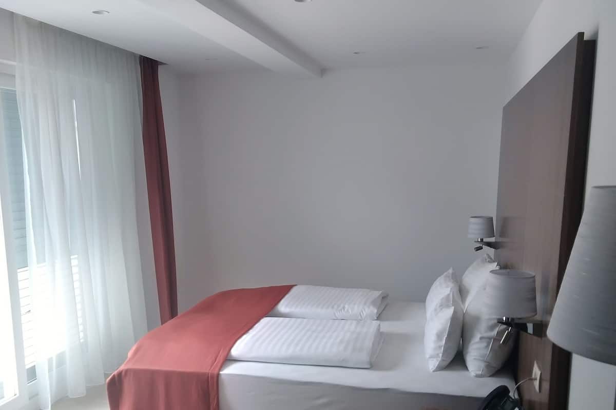 Moderni hotellihuone, jossa on siististi pedattu sänky, yöpöytälamppu, puhelin yöpöydällä ja tuoli.