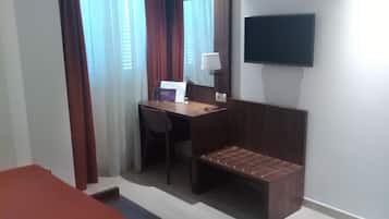 Una habitació d'hotel amb un llit, una taula de nit, una cadira, un televisor i una finestra amb cortines.
