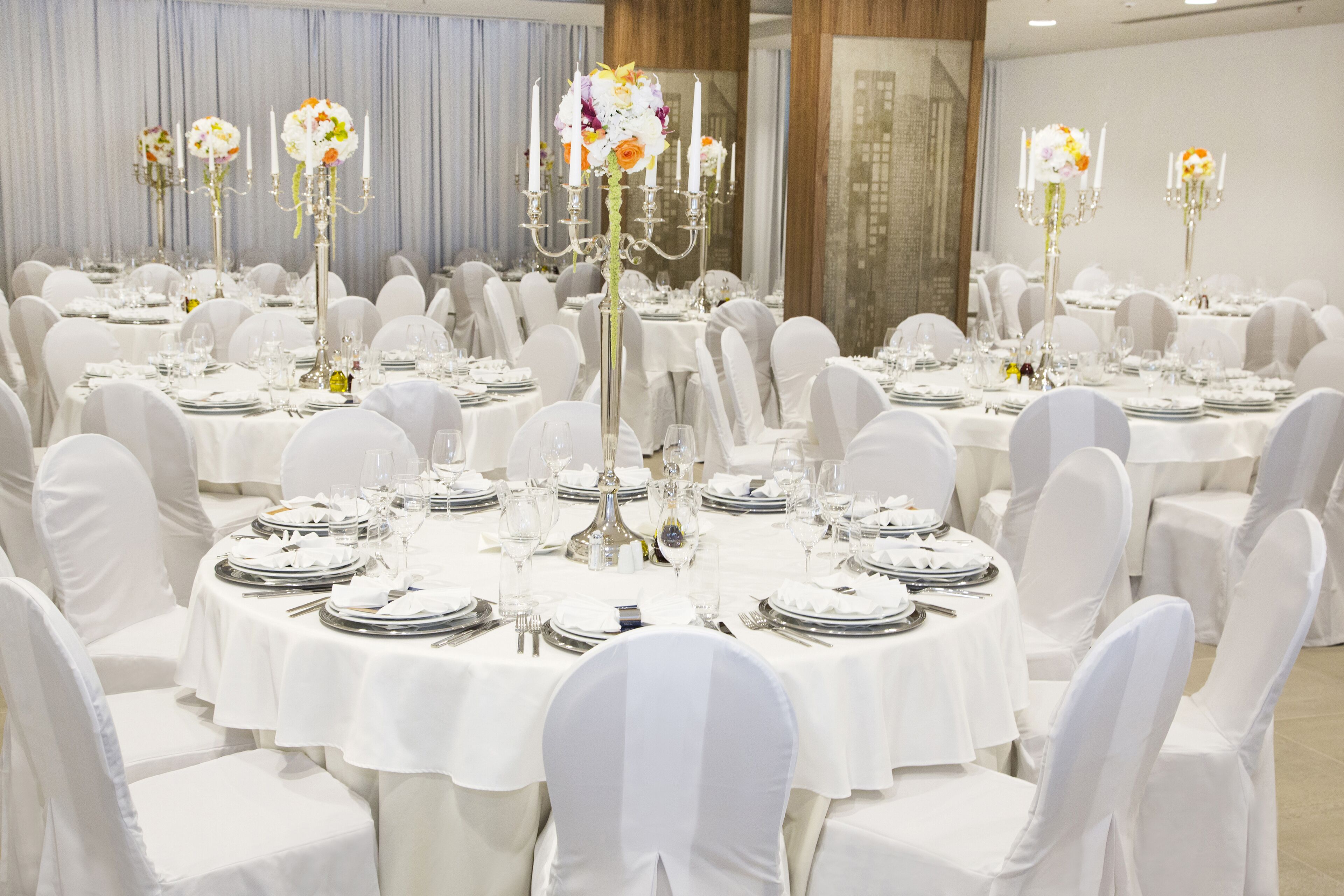 A banquet hall with round tables set for a formal event, each with white tablecloths, silverware, and floral centerpieces.