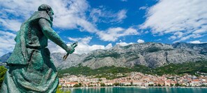 Una estatua que domina un pueblo costero con montañas al fondo.
