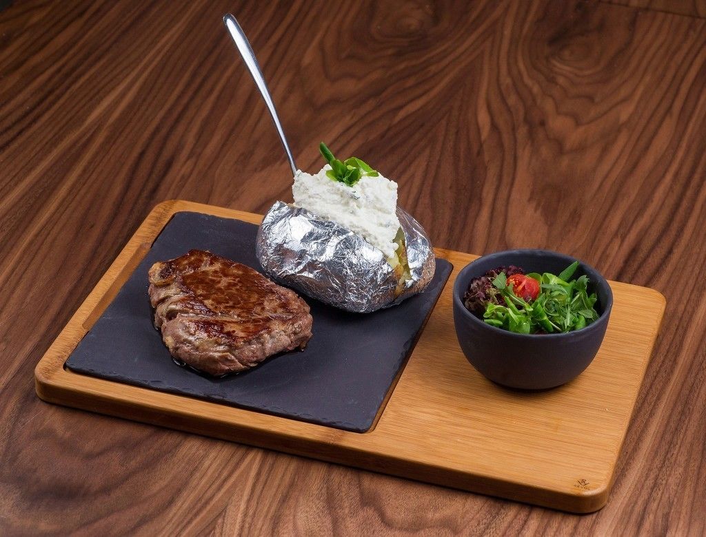 Un repas composé d’un steak, d’une pomme de terre cuite dans du papier d’aluminium et d’une salade, le tout servi sur une planche en bois.