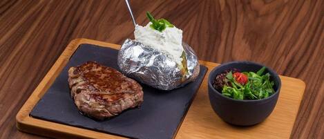 Un repas composé d’un steak, d’une pomme de terre cuite dans du papier d’aluminium et d’une salade, le tout servi sur une planche en bois.
