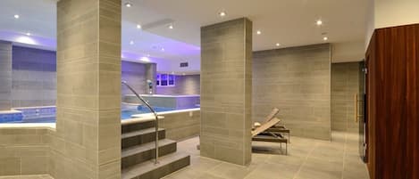 Un área de spa moderna con un jacuzzi, paredes de azulejos y un banco de madera.