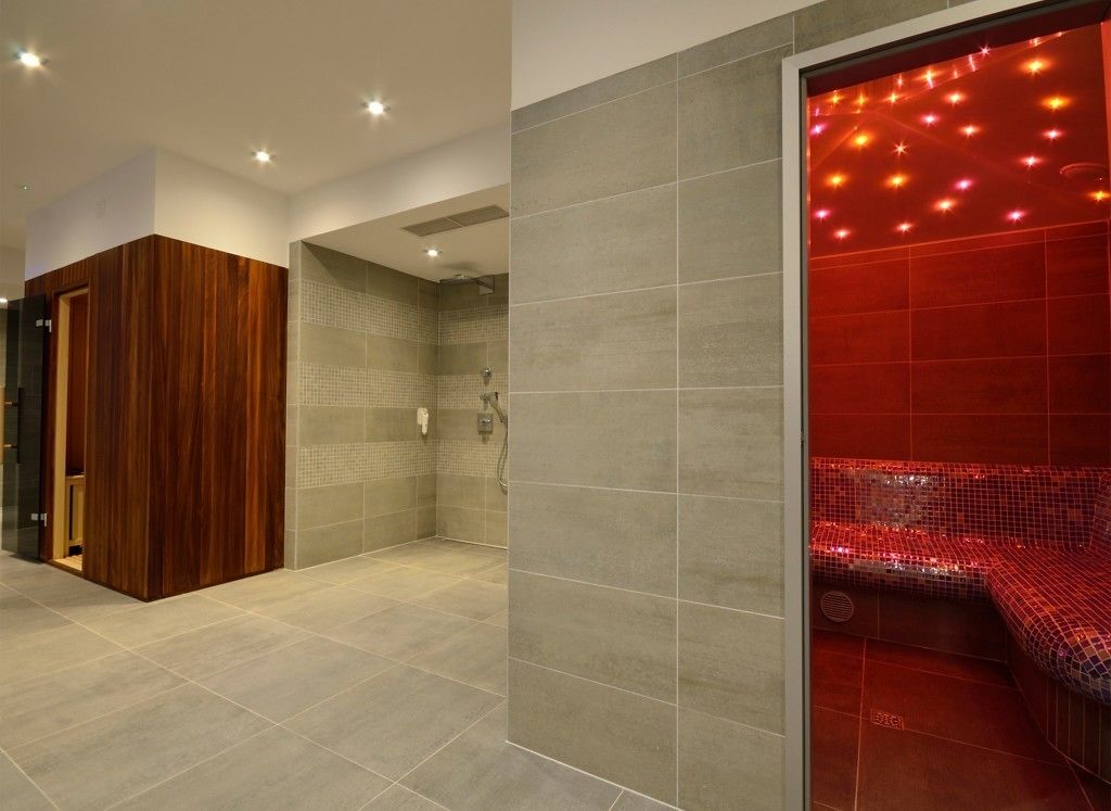 A modern bathroom with a shower area, a wooden vanity, and a red mosaic wall.