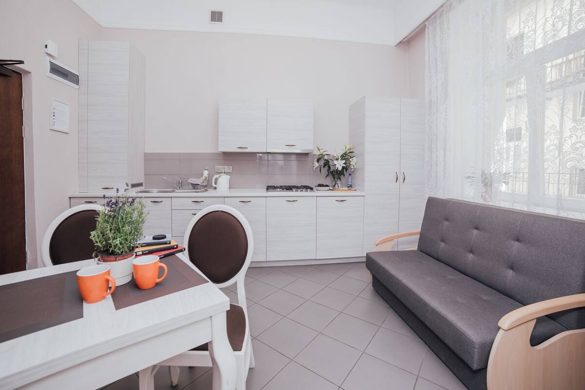 Una cocina moderna con armarios blancos, una mesa de comedor con dos tazas naranjas y un sofá gris.