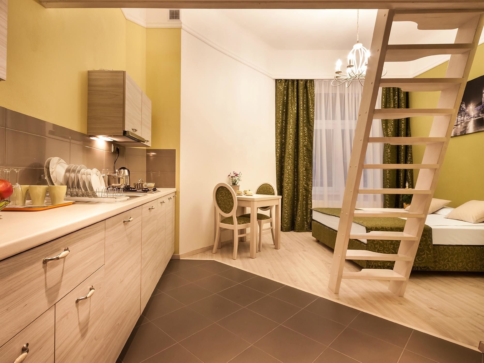 A compact hotel room with a kitchen area, a dining table, a ladder, and a bed.