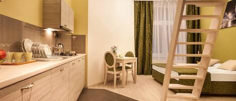 A compact hotel room with a kitchen area, a dining table, a ladder, and a bed.