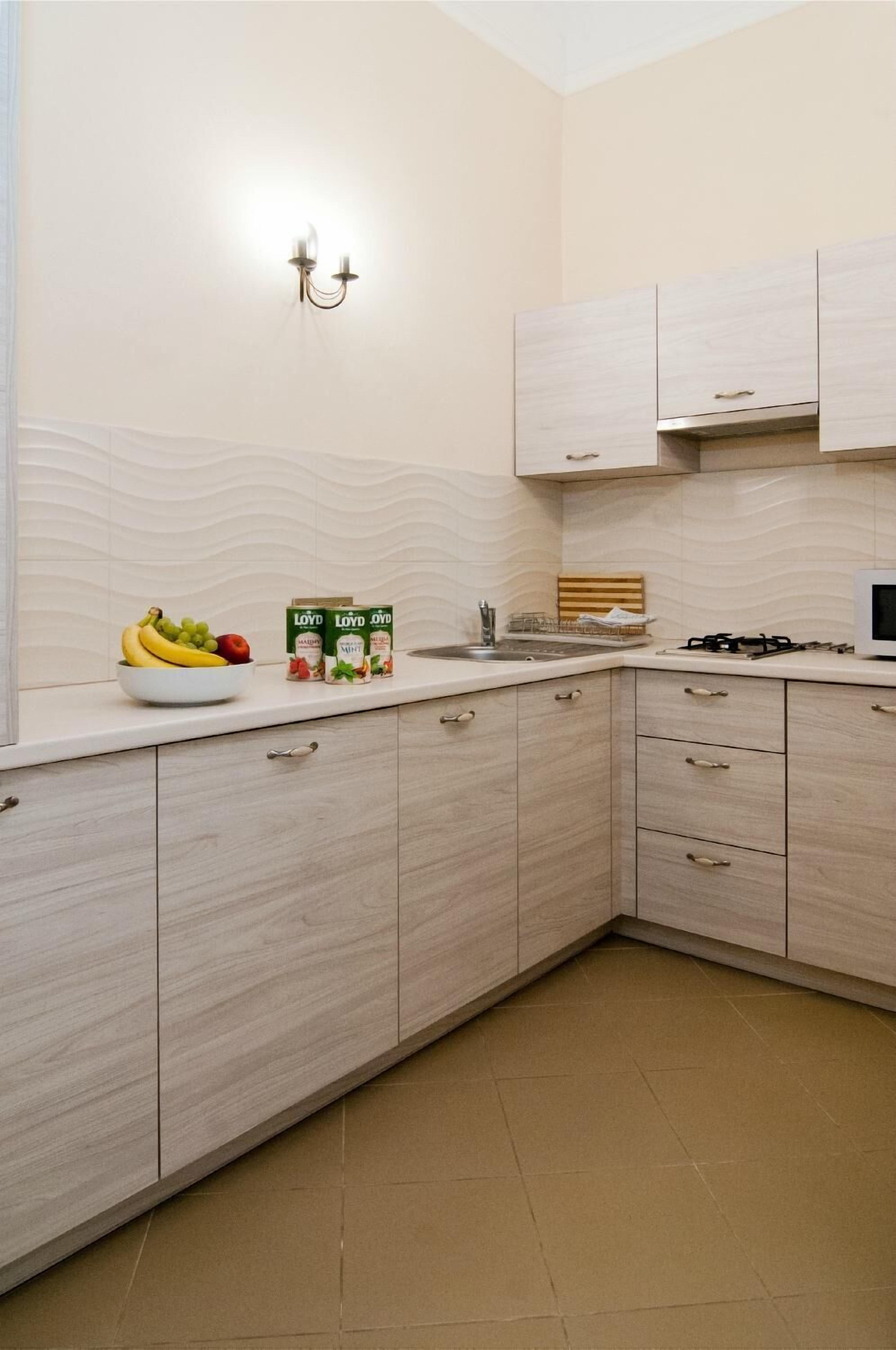 A kitchen with light wood cabinets, a white countertop, a fruit bowl, and a stove.