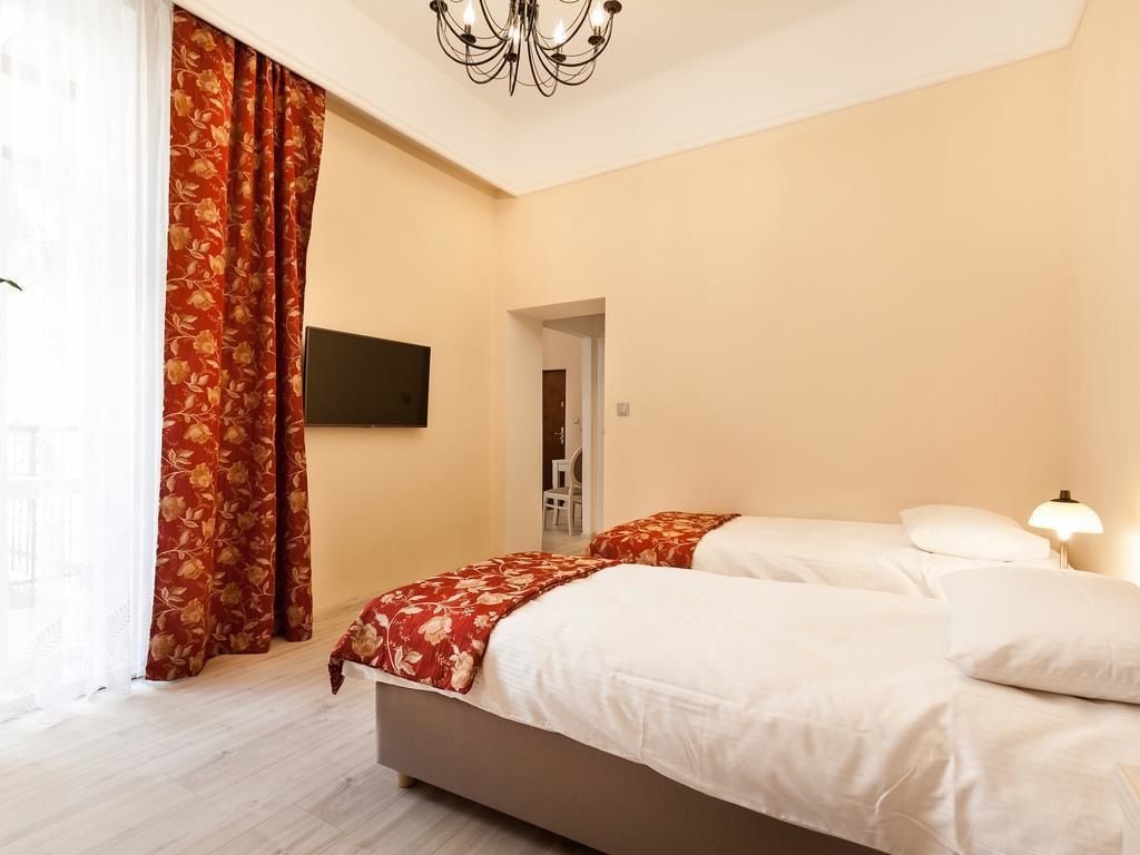 A hotel room with two beds, a TV mounted on the wall, and a chandelier.