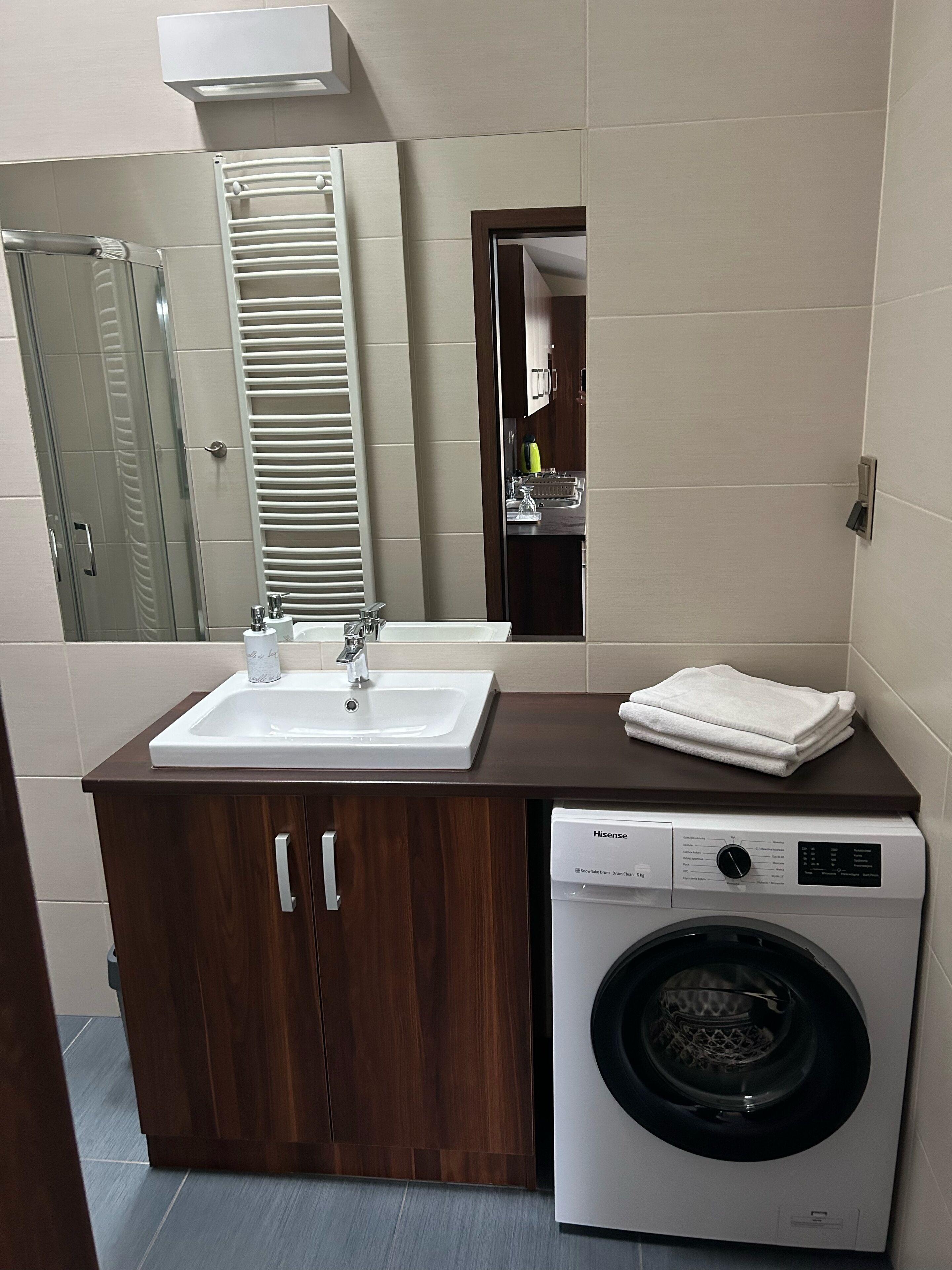 A modern bathroom with a sink, mirror, and a front-loading washing machine.