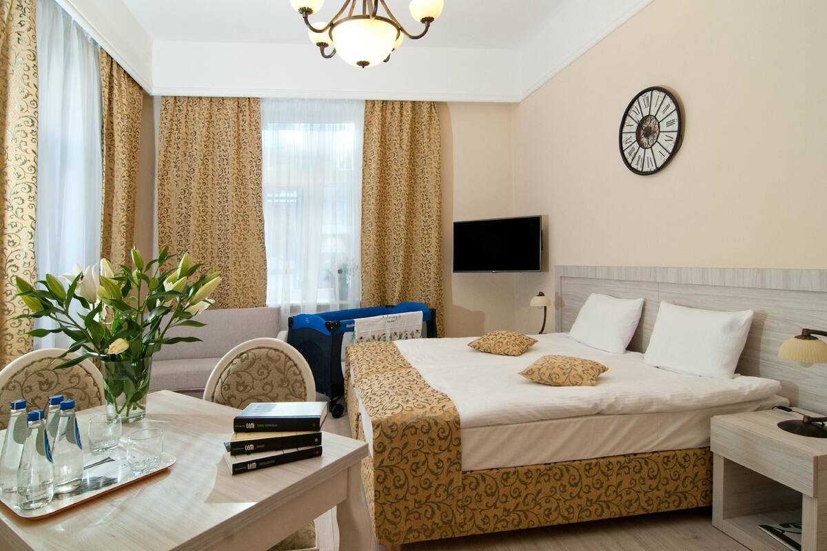 Una habitación de hotel con cama, mesita de noche, televisor y un reloj en la pared.