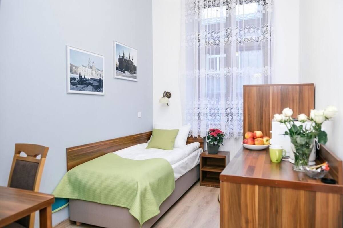 Un dormitorio ordenado con una cama, una mesita de noche con un jarrón de flores, un frutero y dos cuadros en la pared.