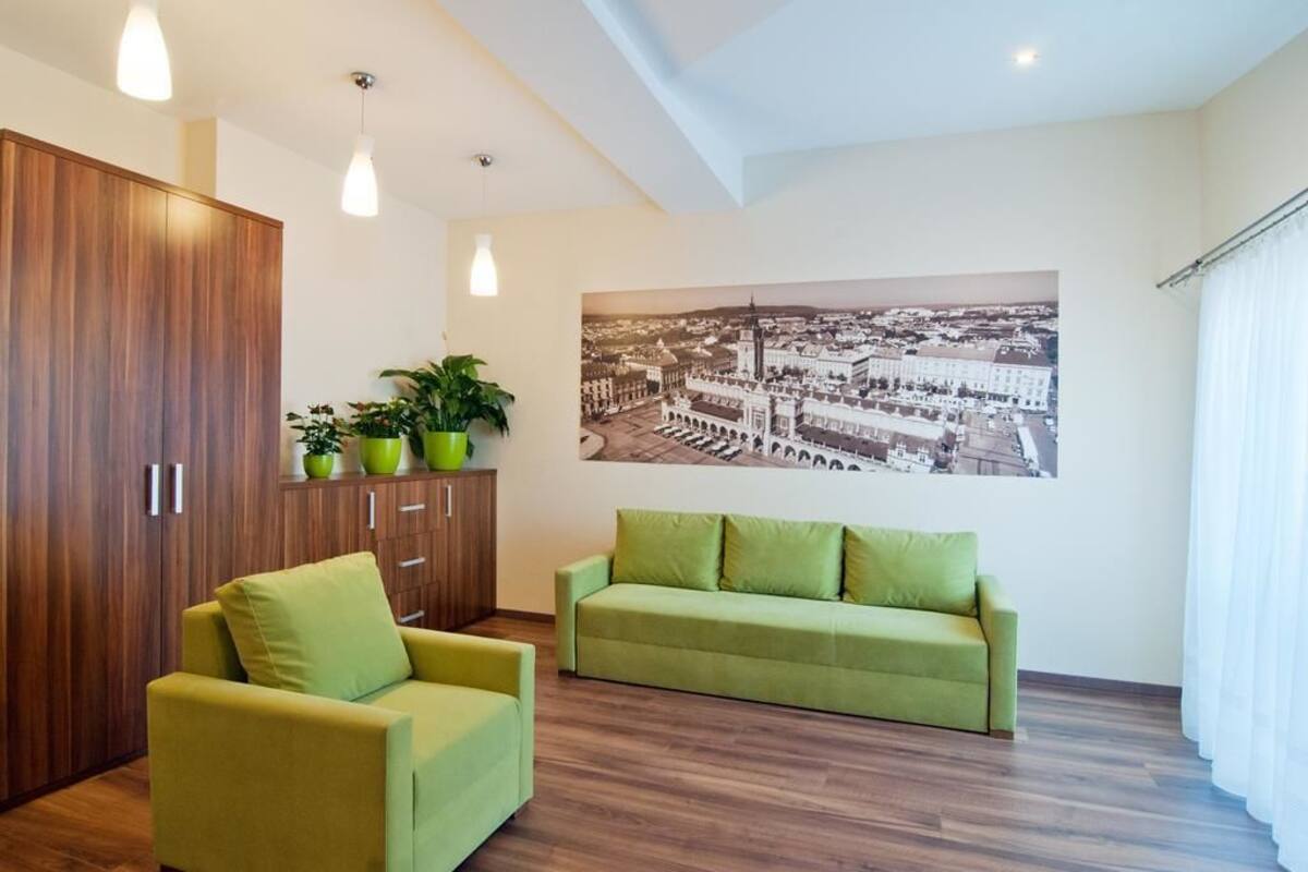 Una sala de estar moderna con un armario de madera, dos sofás verdes, un cuadro grande con una vista urbana y una planta en maceta sobre una estantería.