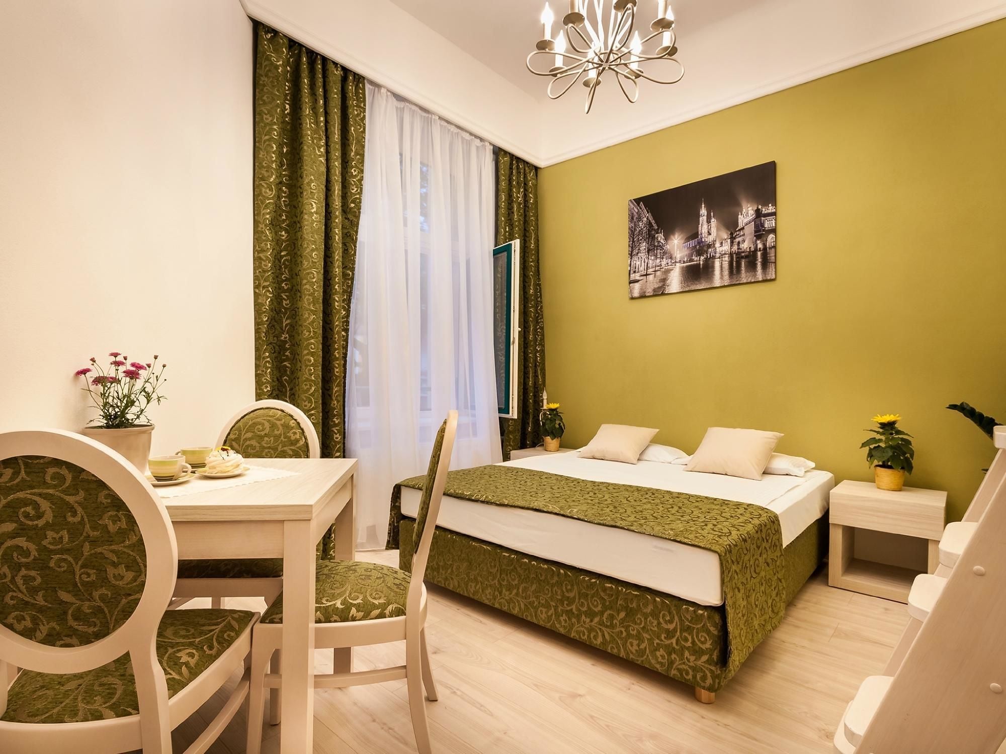 Habitación de hotel con cama, escritorio con silla, una mesita con un jarrón de flores y una mesita de noche con lámpara.