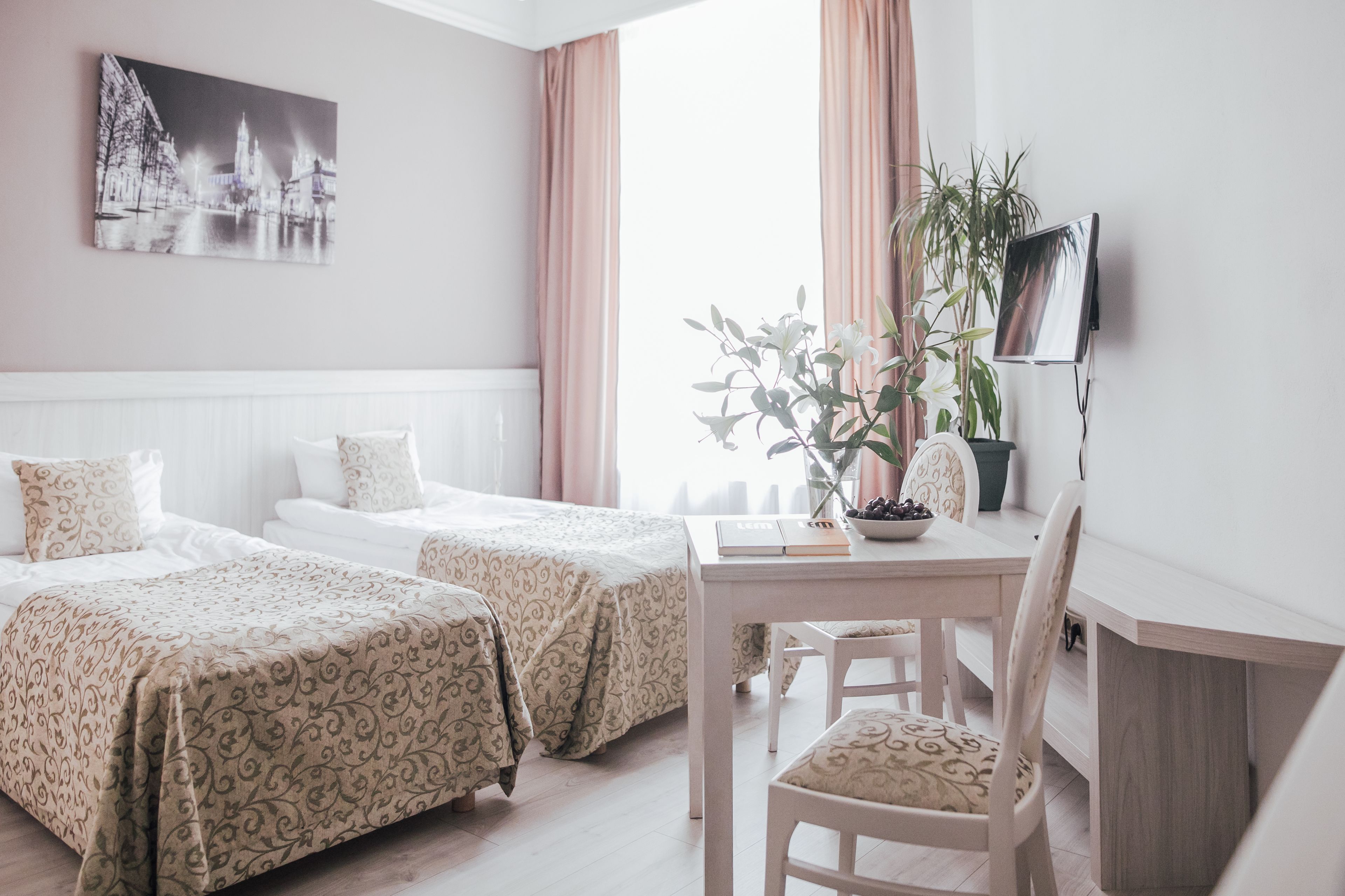 Une chambre d’hôtel avec deux lits, un bureau avec une chaise, une plante en pot et un tableau au mur.