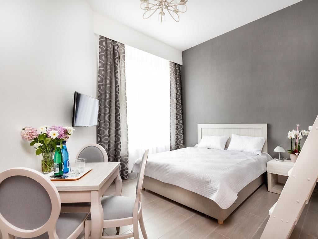 A modern hotel room with a bed, a desk with chairs, a TV, and a window with curtains.