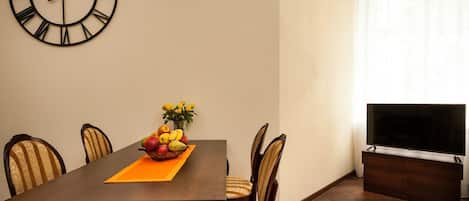 Uma sala de jantar com uma mesa de madeira, quatro cadeiras, uma cesta de frutas e um relógio de parede.