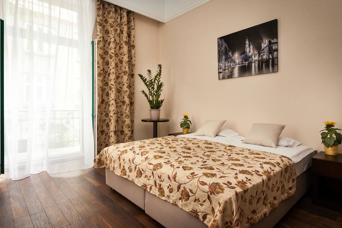 Un dormitorio con una cama grande, una planta en maceta, un cuadro en la pared y vistas a un edificio.