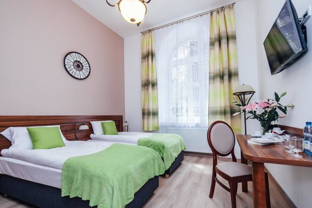 Habitación de hotel con dos camas, un escritorio con silla, un reloj en la pared y una ventana con cortinas.