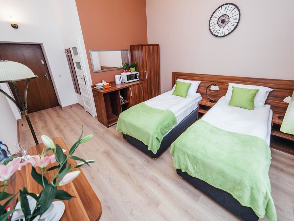 Habitación de hotel con dos camas, un escritorio, un microondas y un reloj en la pared.