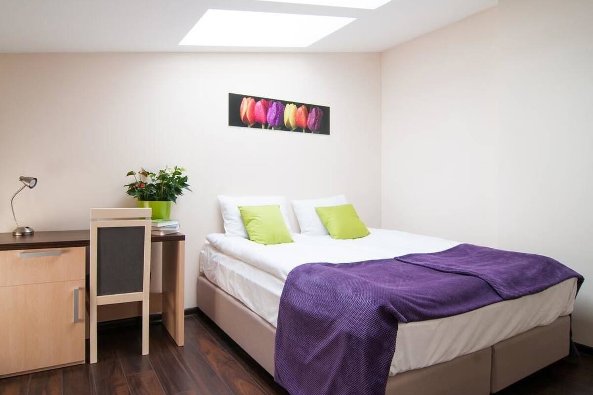 Un dormitorio con una cama, un escritorio, una silla, una planta en maceta y un cuadro colgado en la pared.