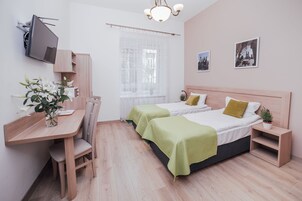 Una camera da letto moderna con una scrivania in legno, due letti con lenzuola verdi, una TV montata a parete e una finestra con tende leggere.