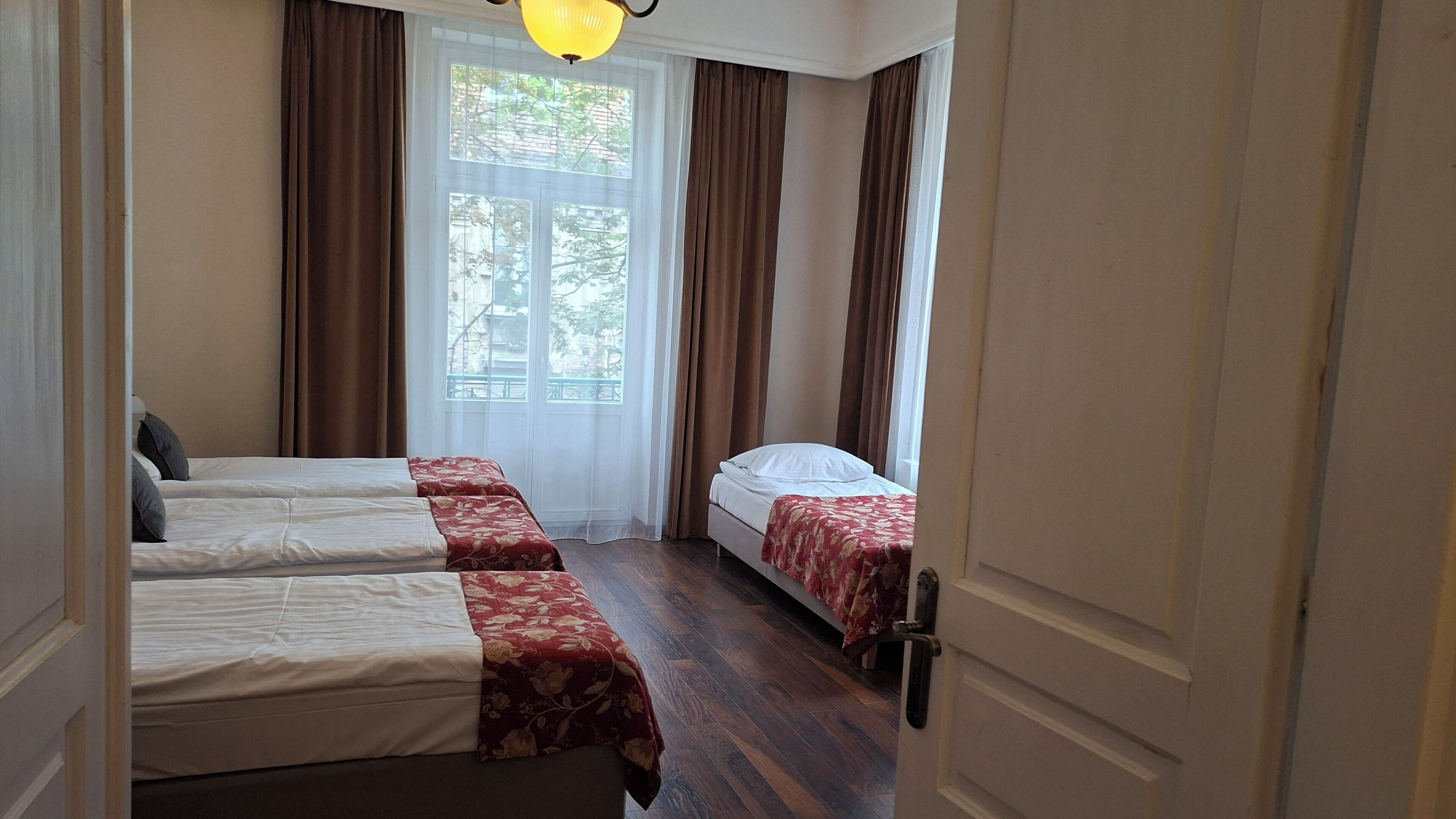 Ein Hotelzimmer mit zwei Betten, einem Fenster mit Vorhängen und einer Tür.