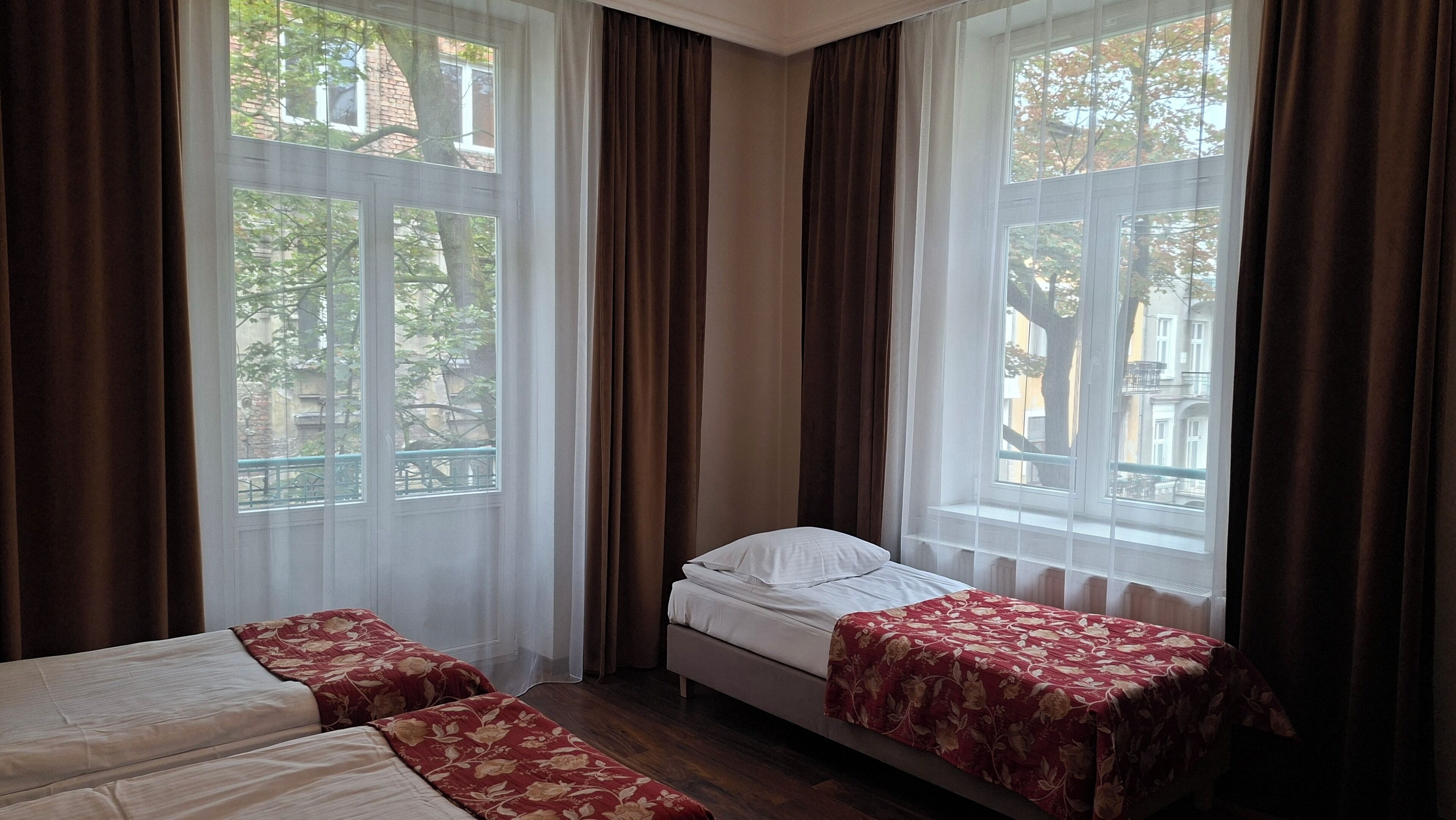 A hotel room with two beds, a window with curtains, and a view of buildings outside.