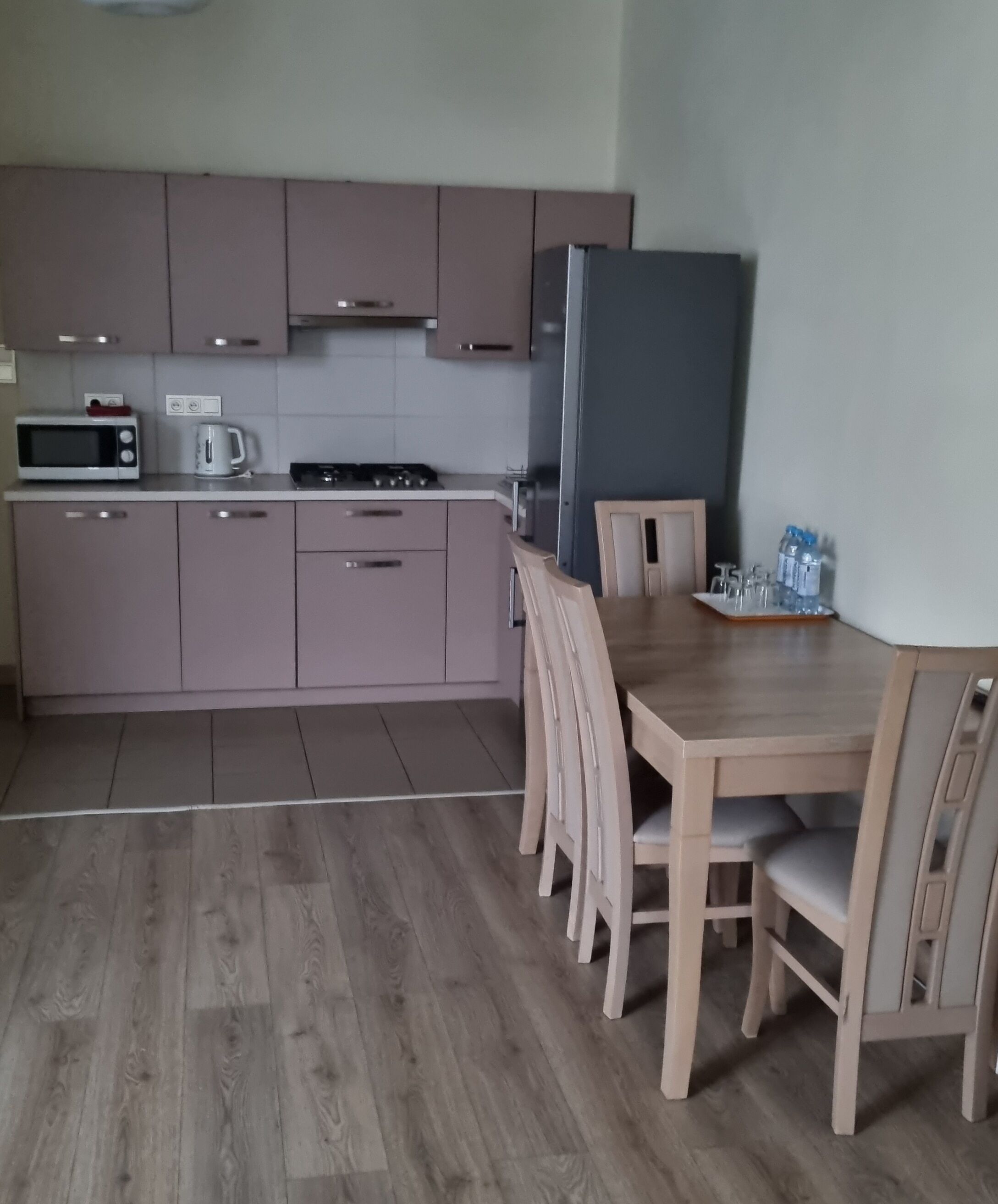 A modern kitchen with wooden cabinets, a microwave, a coffee maker, and a refrigerator. There is a wooden dining table with chairs.