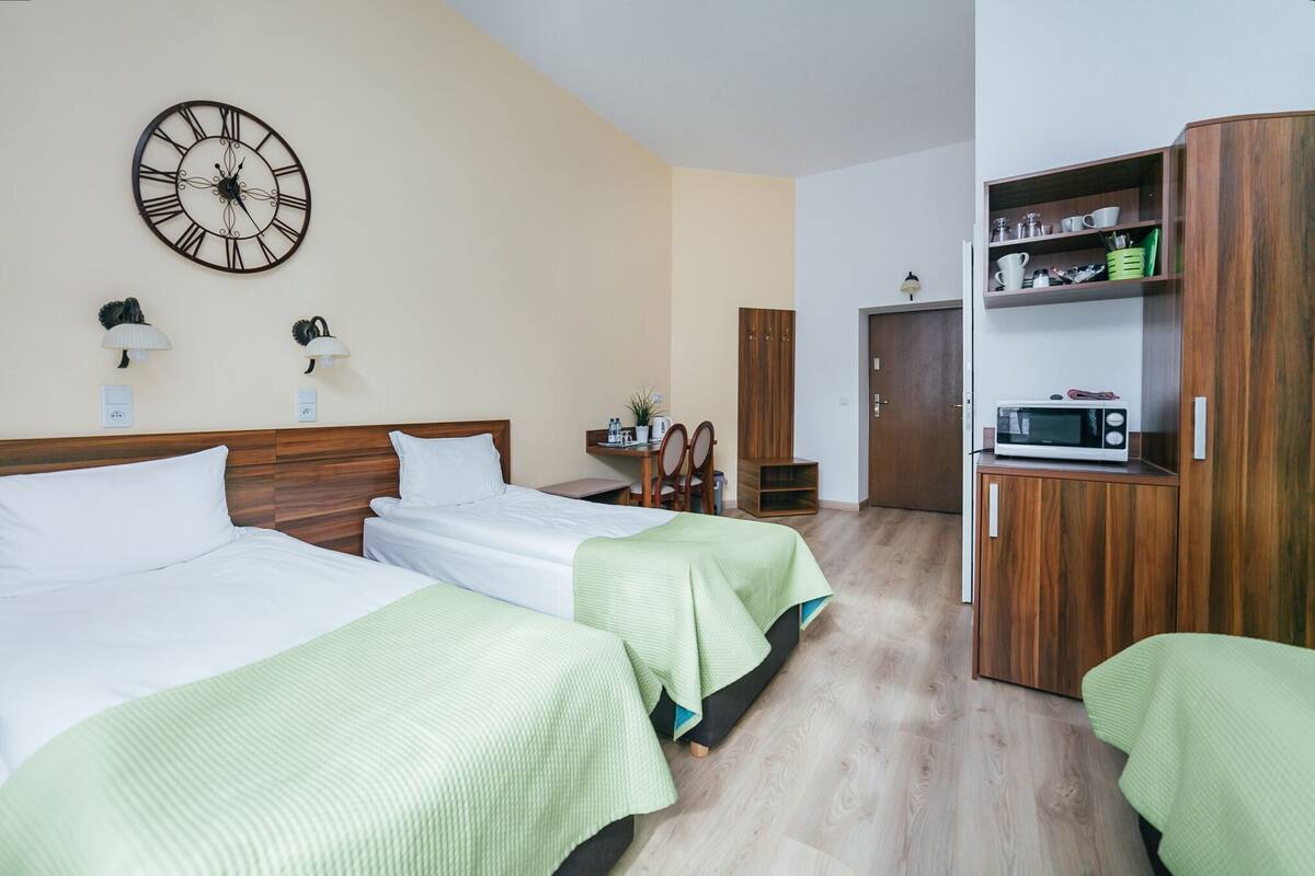 Una habitación de hotel con dos camas, un armario de madera, un microondas y un reloj de pared.