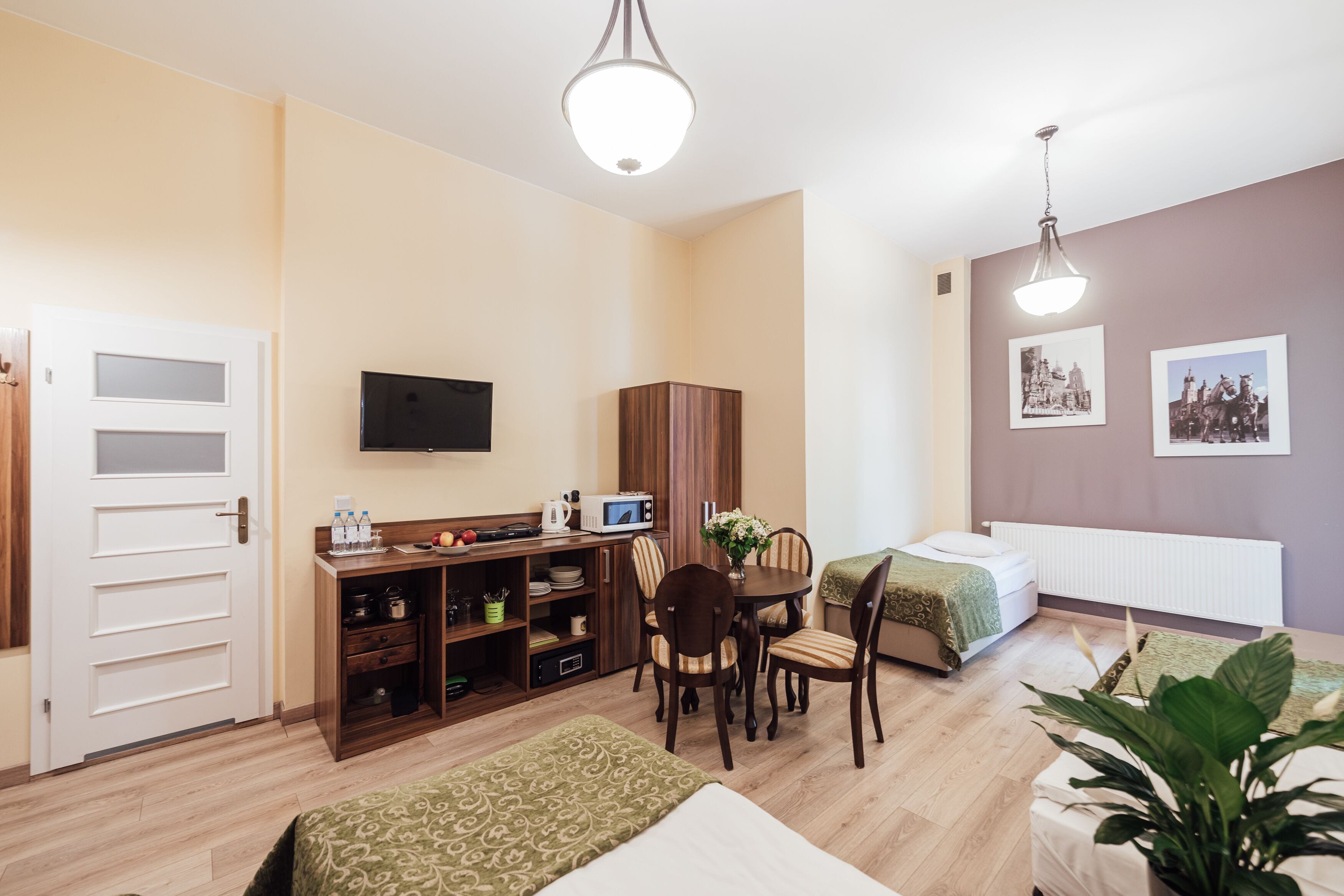 A compact hotel room with a kitchenette, a dining area, a bed, and a TV.