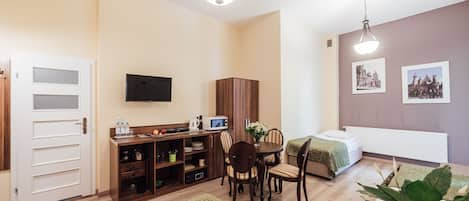 A compact hotel room with a kitchenette, a dining area, a bed, and a TV.