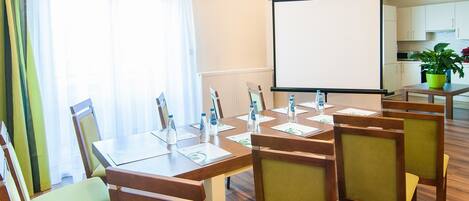 Una sala de conferencias con una mesa grande, sillas, una pantalla de proyector y un ventanal con cortinas.